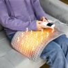 Coussin chauffant utilisé par une femme assise sur un canapé pour chauffer ses cuisses