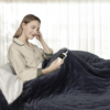 Couverture chauffante électrique noire utilisée par une femme avec télécommande au lit pour un contrôle facile de la température.