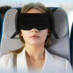 Masque de nuit attaché à un dossier de siège par les sangles de sa bande velcro. Le masque occultant porté par une femme attaché à son tour à la bande velcro lui offre un soutien à 360° et ergonomique dans toutes les directions et dans les transports tous type.
