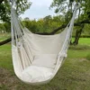 Chaise hamac suspendue crème avec coussin, accrochée à une branche en extérieur