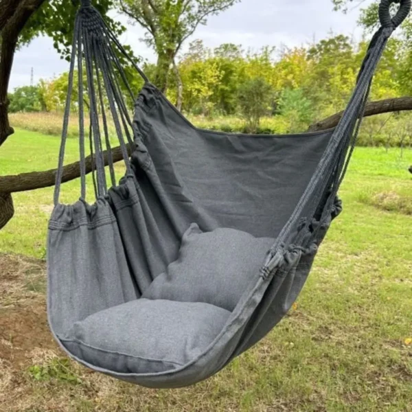 Chaise hamac suspendue grise avec coussin, installée en extérieur sous un arbre